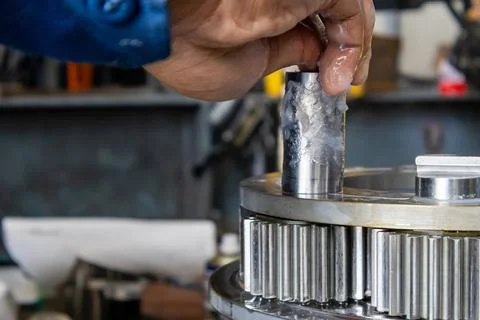 Technician inserts greased pinion pin into planetary gear carrier assembly .. Stock Photos