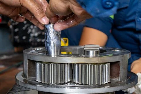 Technician inserts greased pinion pin into planetary gear carrier assembly .. Stock Photos