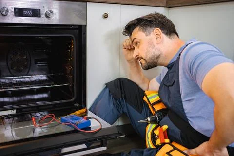 Technician inspecting a broken oven with a multimeter Stock Photos