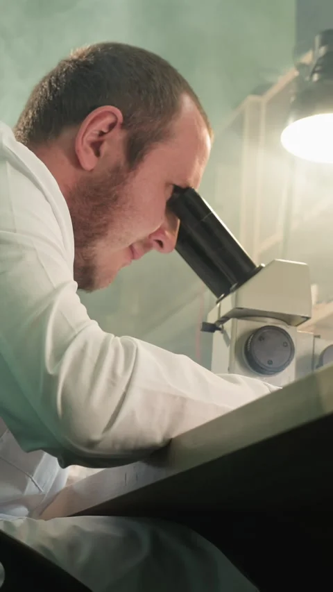 Technician Inspecting Circuit Board Under Microscope in Detailed Workspace Stock Footage 310490636