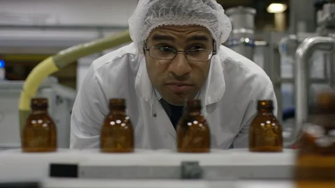 Technician inspecting empty bottles on production line in cosmetic factory Stock Footage 107985891