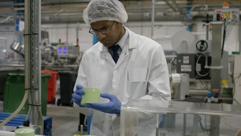 Technician inspecting packed cosmetic boxes on conveyor belt in factory Stock Footage 107959286
