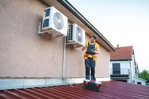 Technician installing air conditioning units using smartphone on a roof Stock Photos