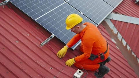 Technician installing solar panels on a red metal roof Stock Footage 343895093