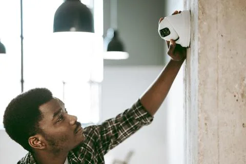 Technician installs security camera on a concrete wall in a modern office Stock Photos