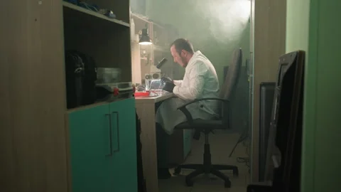 Technician in Lab Coat Working Under Microscope in Smoke-Filled Lab Stock Footage 285405183