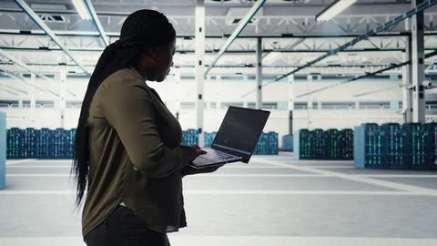 Technician with laptop walks through data center server rows Stockfoto's