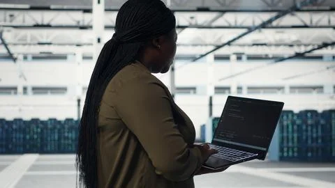 Technician with laptop walks through data center server rows Stockfoto's