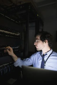 Technician with laptop working at server panel in dark server room Foto stock