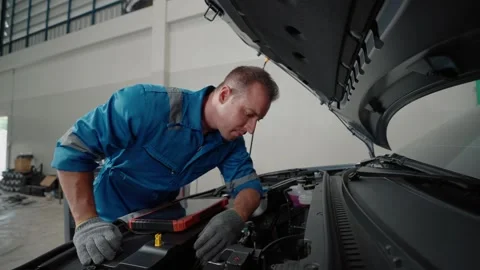 Technician leans over EV car engine, focused and attentive Stock Footage 338332479