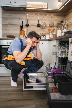 Technician looking stressed while repairing dishwasher in kitchen Stock Photos