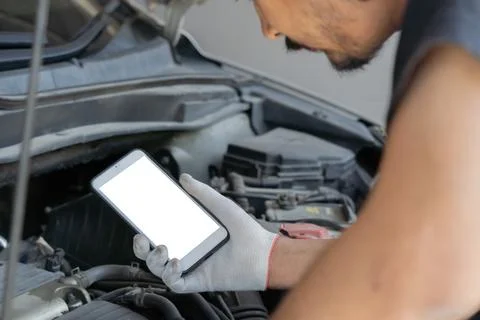 Technician man checking car engine and holding smartphone with isolate scre.. Stock Photos