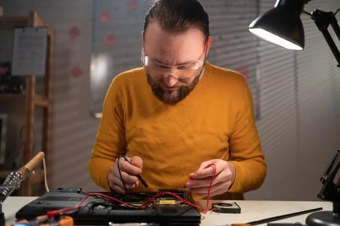Technician man measuring electrical voltage of laptop computer mainboard by u Stock Photos