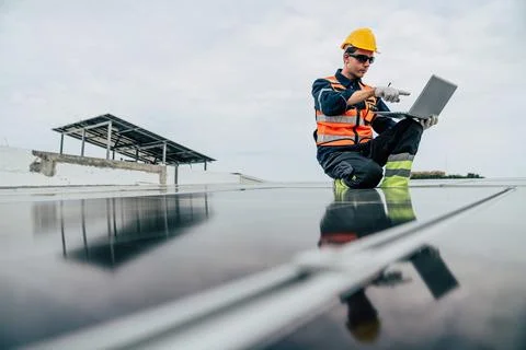 Technician monitors solar panels while sitting on a rooftop during a cloudy.. Stock Photos