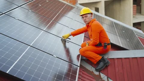Technician in orange uniform cleaning solar panels on a rooftop 库存影片 343894608