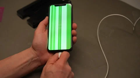 Technician plugging charging cable into broken smartphone showing green screen Stock Footage 306893372