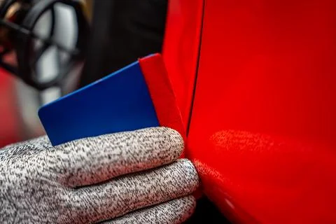 Technician presses squeegee along panel gap of glossy red luxury car Foto stock