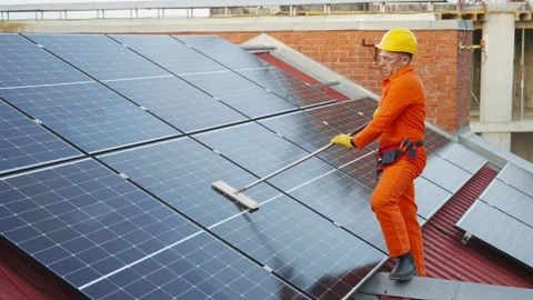 Technician in protective workwear cleaning solar panels on a roof Stock Footage 343894796