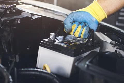 Technician is pulling up an car old battery for replacement Stock Photos