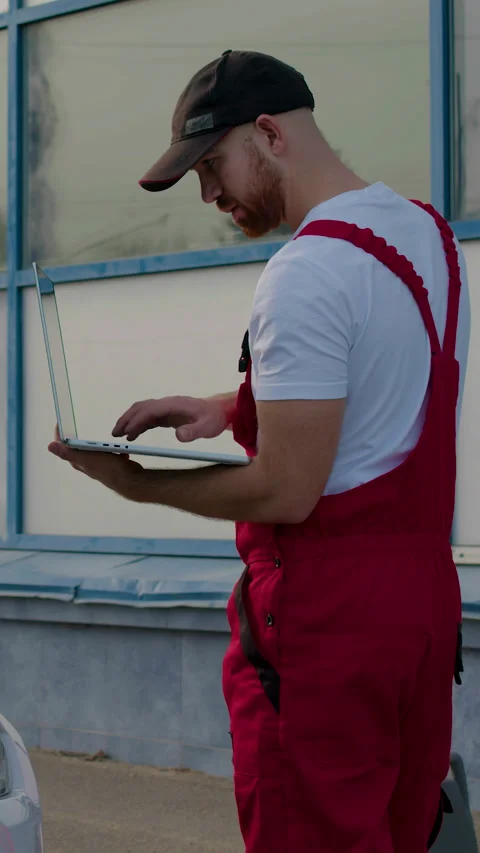 Technician in red overalls using diagnostic computer to troubleshoot engine Stock Footage 318346486