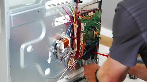 Technician replacing electronic control board inside disassembled electric oven Stock Footage 345658174
