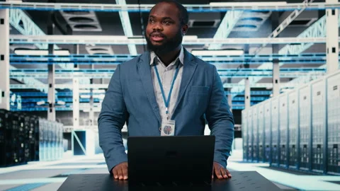 Technician at server room workplace desk using laptop Stock Footage 330030784
