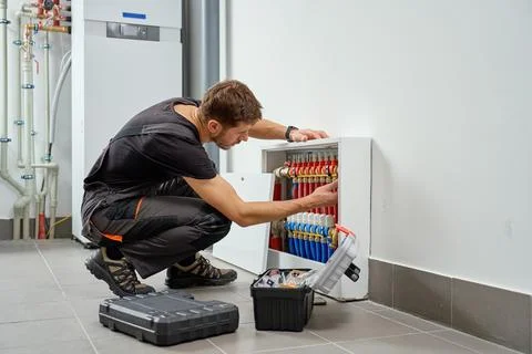 Technician servicing underfloor heating manifold in utility room Stock Photos
