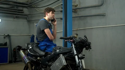 Technician sits on motorcycle and talks on phone Stock Footage 124261339