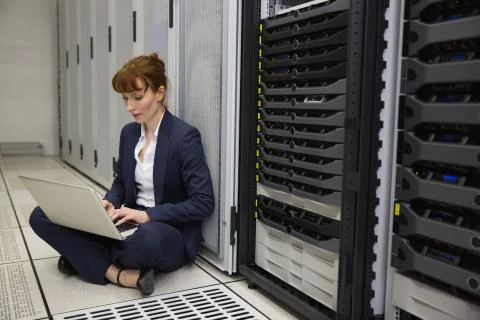 Technician sitting on floor beside server tower using laptop Stock Photos