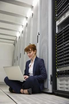 Technician sitting on floor beside server tower using laptop Stock Photos