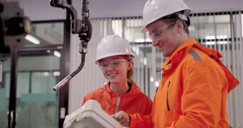 Technician team in orange uniform programming industrial robotic welding arm Stock Footage 314307389