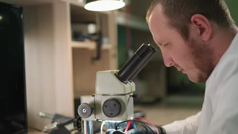 Technician Testing Circuit Under Microscope with Voltmeter in Lab Stock Footage 282298450