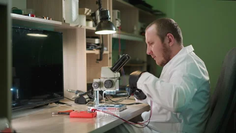 Technician Testing Circuit Under Microscope With a Voltmeter in His Laboratory Video stock 286315457