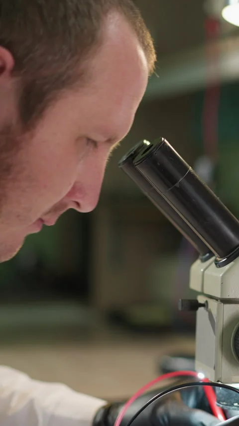 Technician Testing Circuit Under Microscope with Voltmeter in Lab Stock Footage 310489340