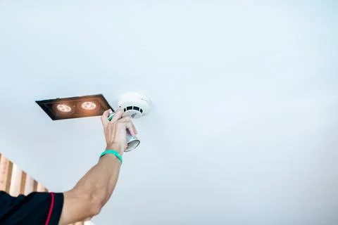 Technician testing smoke detector on ceiling with specialized aerosol spray c Foto stock