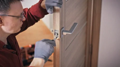 A technician in uniform and glasses methodically repairs an interior door lo Stock Footage 344876512