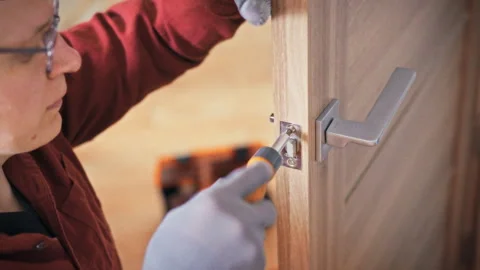 A technician in uniform and gloves repairs door lock on a wooden interior do Stock Footage 342240249