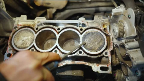 Technician uses screwdriver to remove carbon deposits from engine piston due to Stock Footage 325592495
