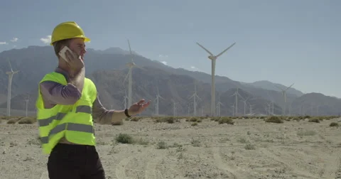 Technician using cellphone in front of a wind farm 4K Stock Footage 63779458