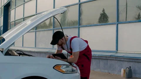 Technician using diagnostic computer to identify engine problems on a white car Stock Footage 312517063