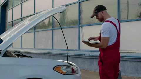 Technician using diagnostic computer to identify engine problems on a white car Stock Footage 312517127