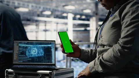 Technician using green screen smartphone in server hub while optimizing AI 스톡 사진