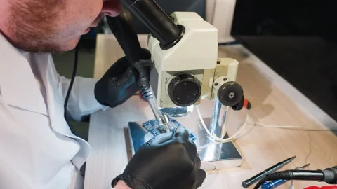 Technician Using Microscope and Soldering Tools to Repair Circuit Board Stock Footage 286315933