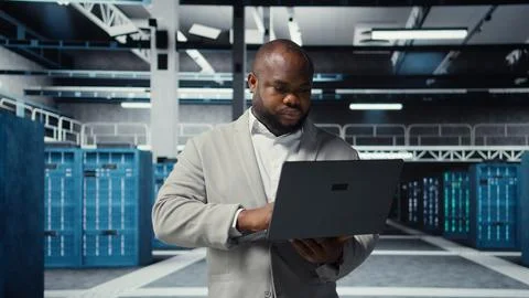 Technician walking in data center, using laptop to check hardware Stock Photos