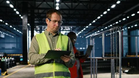 Technician in a warehouse inspects metal components with tablet Stock Photos
