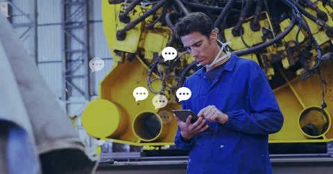 Technician wearing coverall checking tablet in factory, with yellow machine, Stock Photos