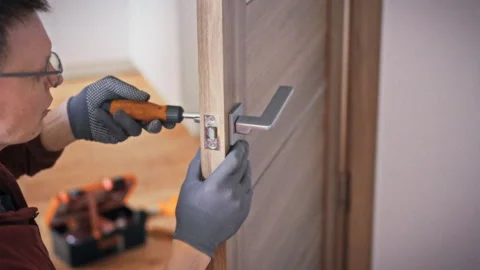 A technician in work uniform and glasses fixes an interior door handle with Vidéo 341489410