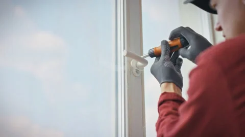 A technician in work uniform and gloves removes a plastic window handle usin Stock Footage 343858649