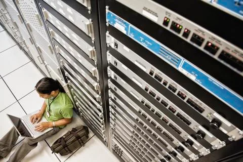Technician working on a laptop computer while doing diagnostic work on a server 스톡 사진