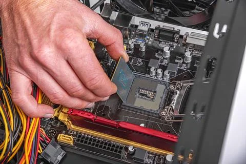 A technicians hand installs a central processing unit into the socket of a Stock Photos